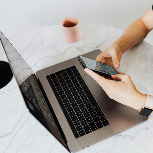 Man typing on phone infront of laptop
